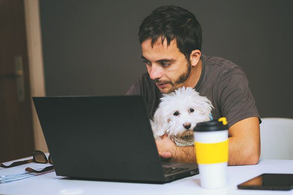 Man holding his dog while using laptop